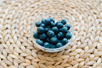 Fototapeta na wymiar fresh ripe blueberries in a glass bowl on a natural wicker napkin made of dry seaweed background. the concept of healthy food, vegan food