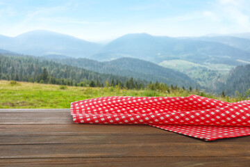 Picnic wooden table with checkered red napkin and picturesque landscape on background