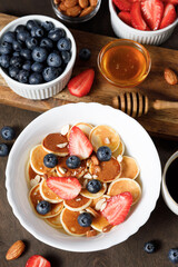 Mini pancakes cereal bowl with berries on wooden background