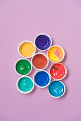 Open jars with gouache on a pink background. The view from the top. Variety of colors. Background, texture.