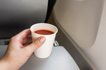 .Woman passenger holding paper cup of tomato juice sitting in the plane armchair. Lunch for airline...