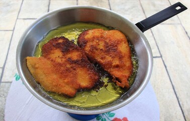Frying chicken schnitzel in a pan with hot olive oil. Selective focus