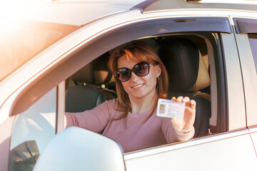 Getting a driver's license, a beautiful driving girl shows a new driver's license. Young woman holding driving license near open car.