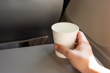 Woman passenger holding paper cup of water sitting in the plane armchair. Lunch for airline passengers on tray table. Dinner meal, beverage on board.