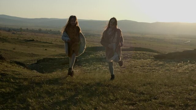 two cute sisters running on hills joyfully in the sunset