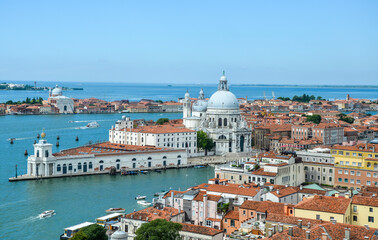 Fototapeta premium Aerial view of the red tiled roofs, Mediterranean Sea and Basilica Santa Maria della Salute standing at the entrance to The Grand Canal in Venice, Italy