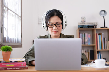 Modern young Asian woman working from home and listening to the music with a white headphones.