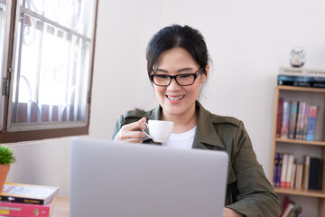 Modern young Asian woman working from home and drinking a coffee with happy and smile.