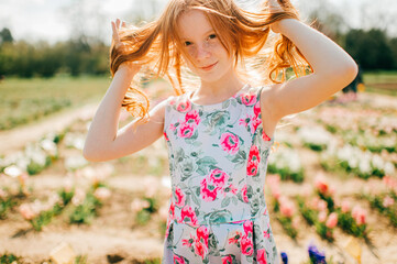Portrait of beautiful young girl with long red hair and pale skin in flowers dress relaxes in the big flower garden
