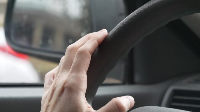 Woman's fingers tapping a steering wheel of a car while she sits at a red light.