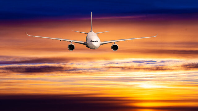 Passengers commercial airplane flying above clouds in sunset light.