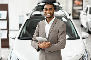 Smiling Dealer Standing Near Luxury Automobile Holding Folder In Showroom