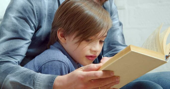 Close up portrait of a little boy with dad reading an interesting book together at home