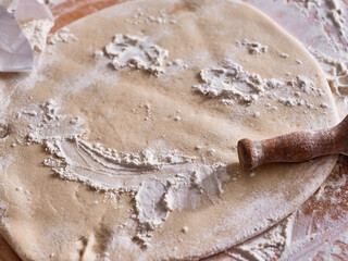Piece of egg pasta dough rolled out on the table with the rolling pin.