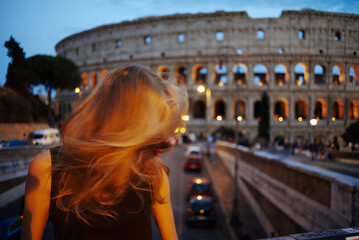 Fototapeta na wymiar Rome, Italy - August 21, 2018. Girl on the background of the Coliseum in the evening. Illuminated Coliseum at dusk, Rome.