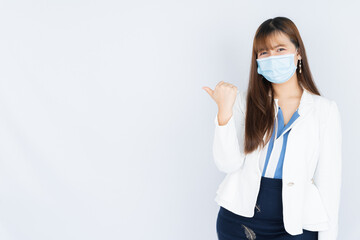 Smiling Asian business woman wearing a medical face mask and pointing finger to side blank space...