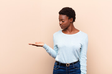 young pretty black womanfeeling happy and smiling casually, looking to an object or concept held on...
