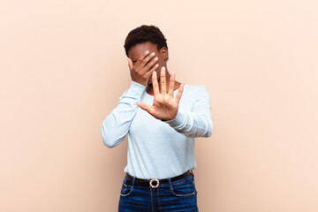 young pretty black womancovering face with hand and putting other hand up front to stop camera,...
