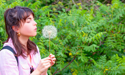 Relaxed young girl in the park blowing dandelion flower seed isolated green background