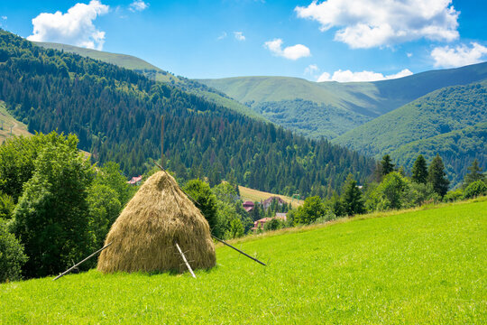 summer landscape of rural valley. Stack of hay on a green meadow in the mountains in the morning under a blue summer sky