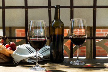 Copas de vino tinto junto a una botella y un racimo de uvas moradas sobre una mesa de madera...