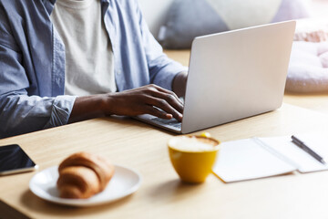 African American blogger working with laptop while having breakfast in cafe, closeup