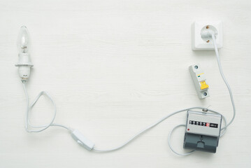 Light bulb with wiring, socket and electric meter on white workbench flat lay background with copy...