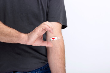 Blood donorship. Man in gray T-shirt hand taped with patch with red heart after giving blood on...