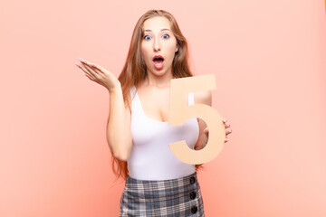 yound blonde woman surprised, shocked, amazed, holding a number 5.