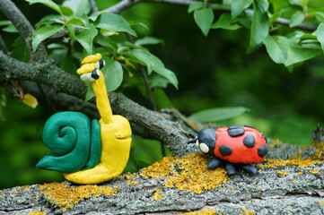 Figurine of a ladybug and a snail made of plasticine on a tree.