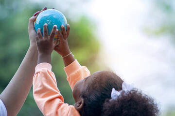 African mixed race girl playing globe model simulation with her mother, both hands lifted the...