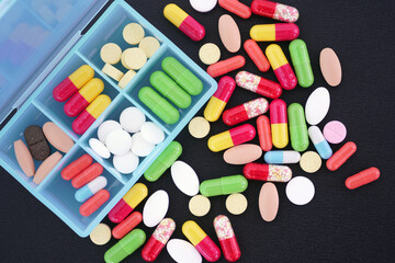 lot of different colorful tablets and capsules on an isolated black background.