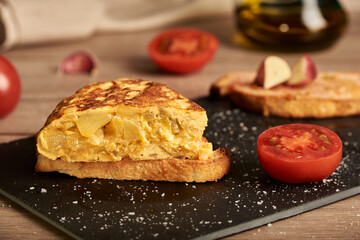 A classic tortilla de patatas, potato omelette snack on a slice of bread. The bread is on a black plate. Typical spanish food.