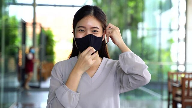 Young optimistic Asian female student giving thumbs up gesture. She's wearing a protective mask (PPE) to avoid air pollution or Corona Virus pandemic for safety.