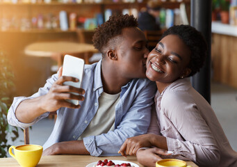 African American man taking selfie while kissing his girlfriend at urban cafe