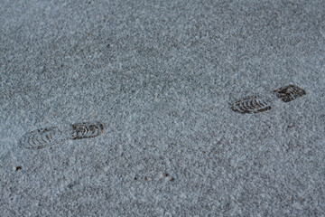 shoeprints on icy ground. Human feet traces, shoes imprints on white snowy road. Fresh snow fallen on asphalt. traces left by man walking away, trajectory of person leaving. several steps