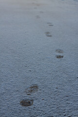 shoeprints on icy ground. Human feet traces, shoes imprints on white snowy road. Fresh snow fallen on asphalt. traces left by man walking away, trajectory of person leaving. several steps