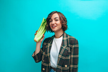 Happy woman holding fresh green celery wearing casual isolated over blue background. Healthy lifestyle concept