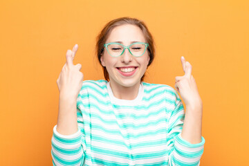 yound blonde woman smiling and anxiously crossing both fingers, feeling worried and wishing or...
