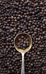 Black pepper grains background with a metal spoon. Composition with black peppercorn and a spoon with copy space for text. Close up