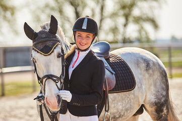 Beautiful horse rider girl stands near a white horse on a farm