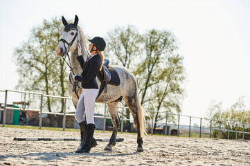 Beautiful horse rider girl stands near a white horse on a farm