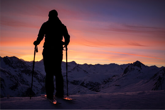 Silhouette d'un homme à ski en train d'admirer le lever de soleil au loin sur les montagnes enneigées à Tignes