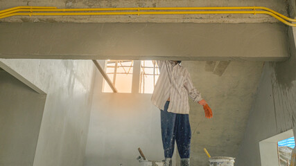 Fototapeta premium female worker plaster liquid cement on wall for new building house. labor mason with orange latex gloves stand on wooden scaffolding use for high level under stair.