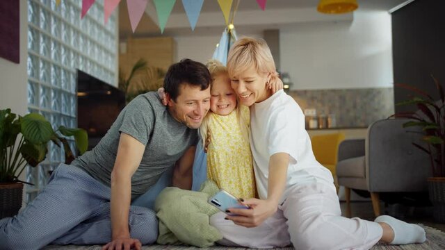 Happy Caucasian family taking selfie photo using front smartphone camera at cozy home, capturing positive moment together casual smiling technology mobile device sharing pleasure lifestyle indoors