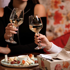 female friends - hands clinking white wine glasses, restaurant or bar on background, close up view. evening, celebration and holidays concept