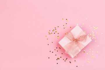Gift or gift box and stars confetti on a pink table from above. Flat composition for birthday