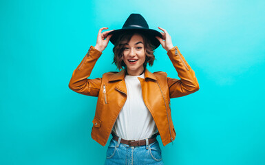 Fashion portrait of young stylish hipster woman wearing trendy brown leather jacket, black hat, blue denim jeans and white blank t-shirt .