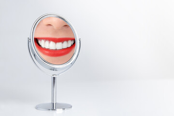 The smile of a young woman with clean and beautiful white teeth Red lips Reflections on the mirror set on the white table. Dental health care concept. copy space.