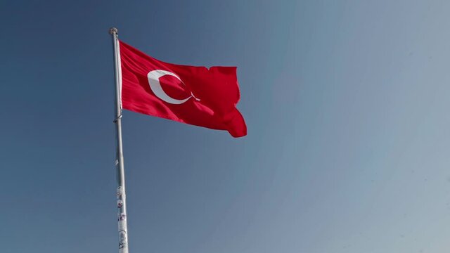Turkish Flag waving in the wind over blue sky. Flag of Turkey; A red flag featuring a white star and crescent often called as moon-star